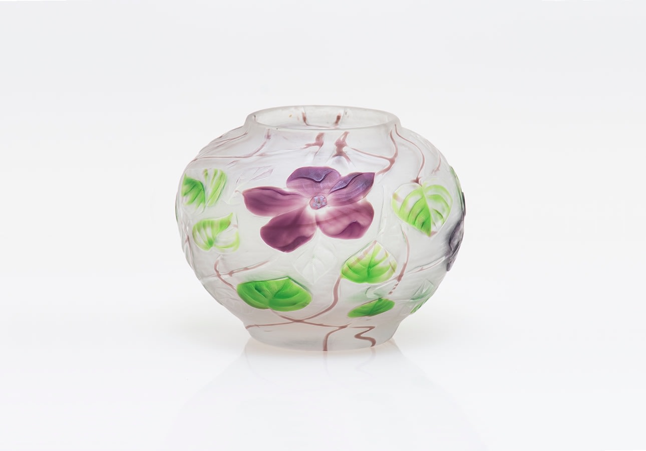 a flattened ovoid tiffany glass vase carved in the cameo technique, with a motif of large purple clematis flowers with green leaves and swirling brown vines standing in low relief from the body of the vase in a frosted opalescent glass intended to replicate the appearance of rock crystal