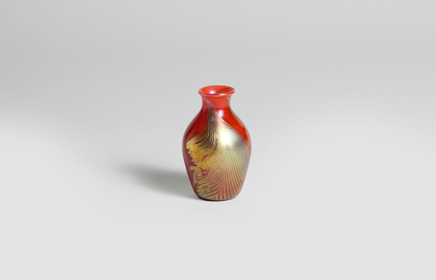 a miniature baluster form cabinet vase in red tiffany glass decorated with a motif of pulled feathers in gold