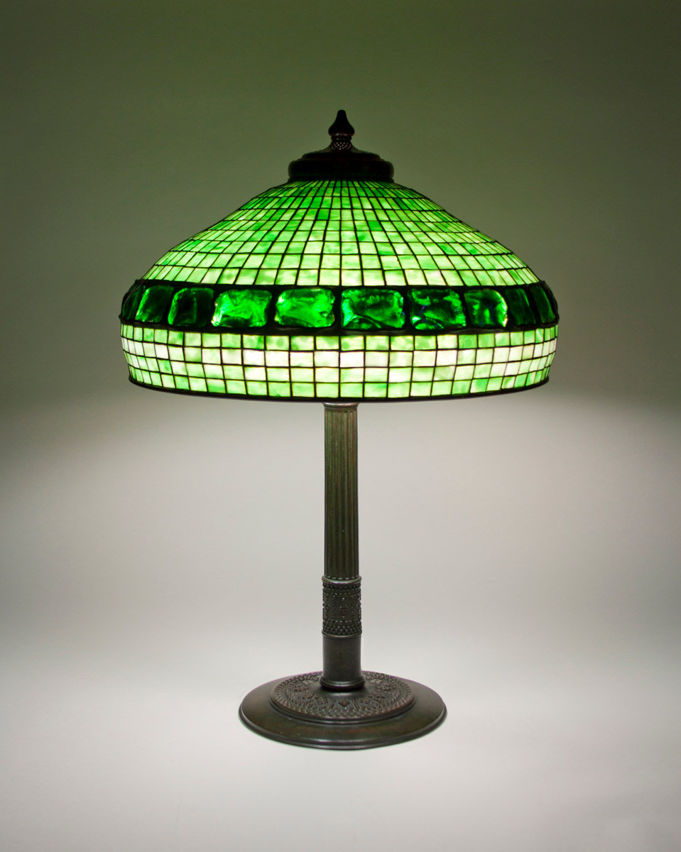 a tiffany lamp, the geometric leaded glass shade in gridded green glass with a horizontal band near the lower edge of iridescent irregularly shaped pressed &quot;turtle back&quot; tiles