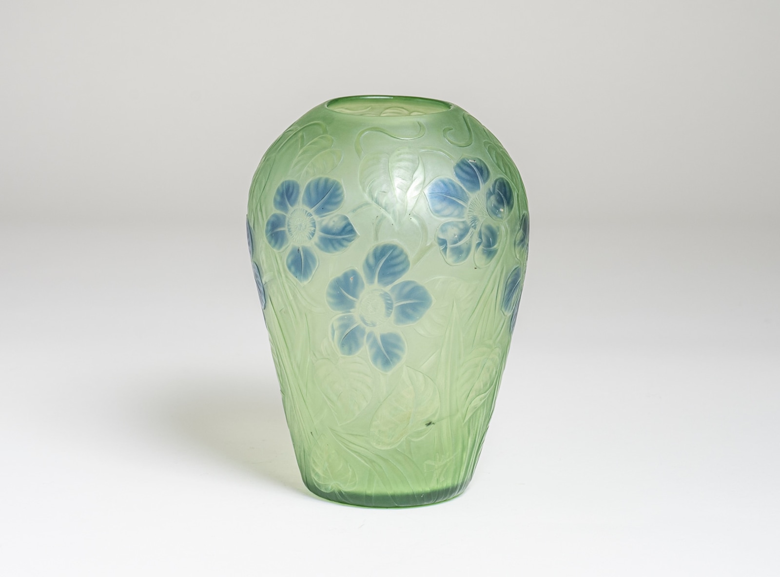 a cameo tiffany favrile glass vase, the green base glass with allover motif of pointed leaves and vines, interspersed near the rounded shoulder with blue five-petaled flowers. All in a soft muted tone.