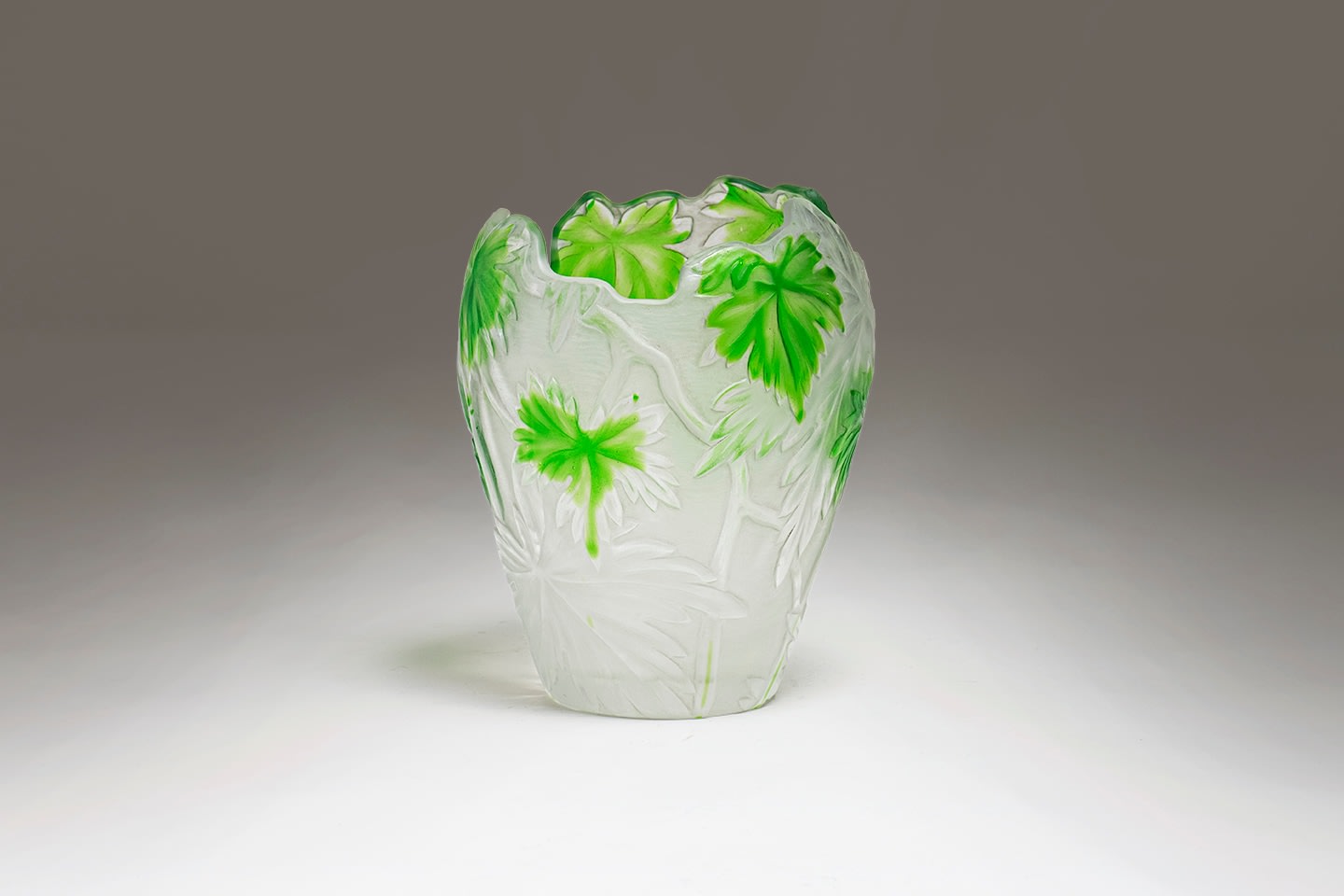 a vase of frosted opalescent glass with light green palmate leaves carved in the cameo style, raised from the surface, the background also carved with leaves, the rim of the vase of irregular shape conforming to the edges of the leaves