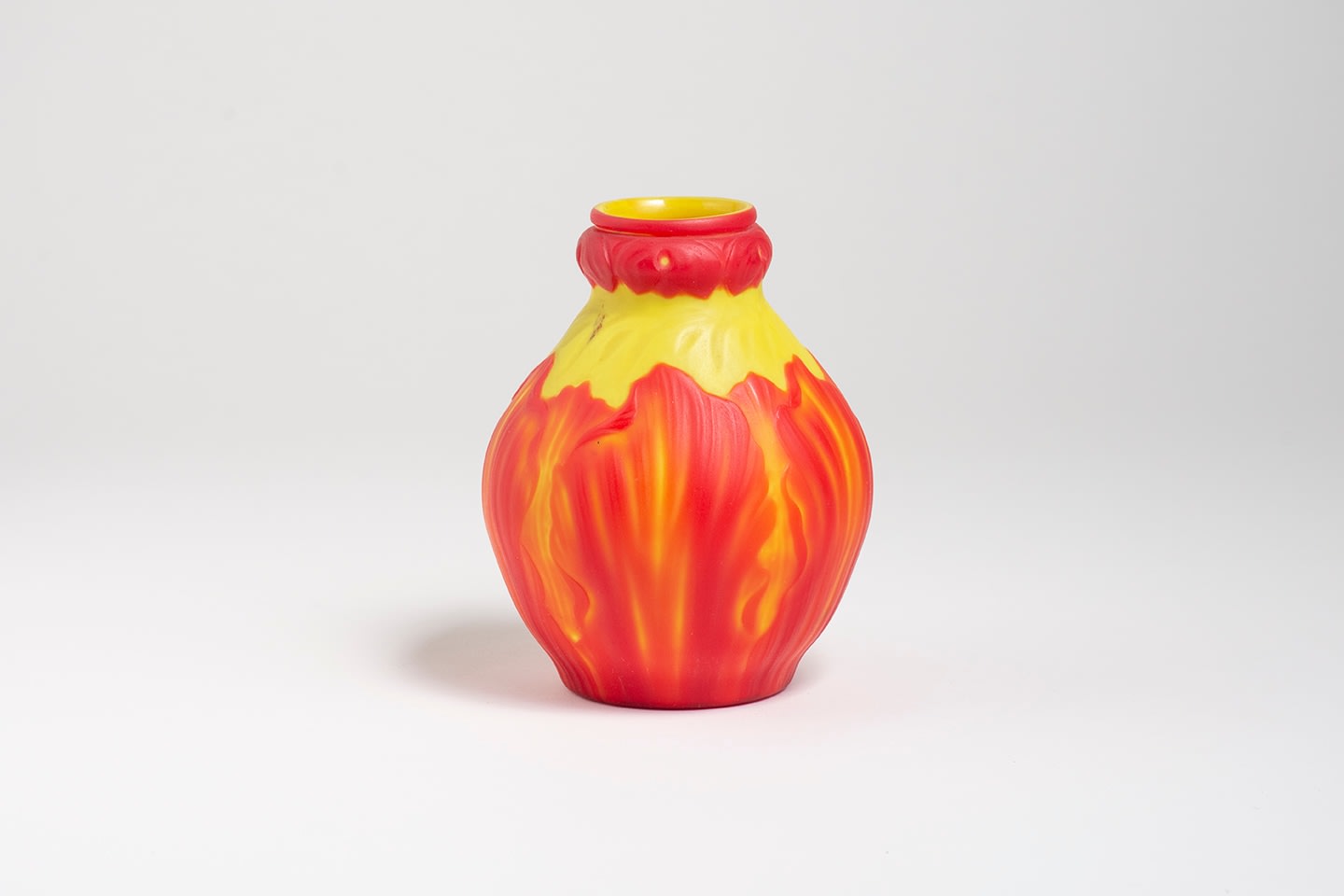 a cabinet vase in the cameo technique by tiffany studios, the base glass in bright yellow, the raised layer of red glass carved in the form of a fancy frilled or broken tulip with curling petals
