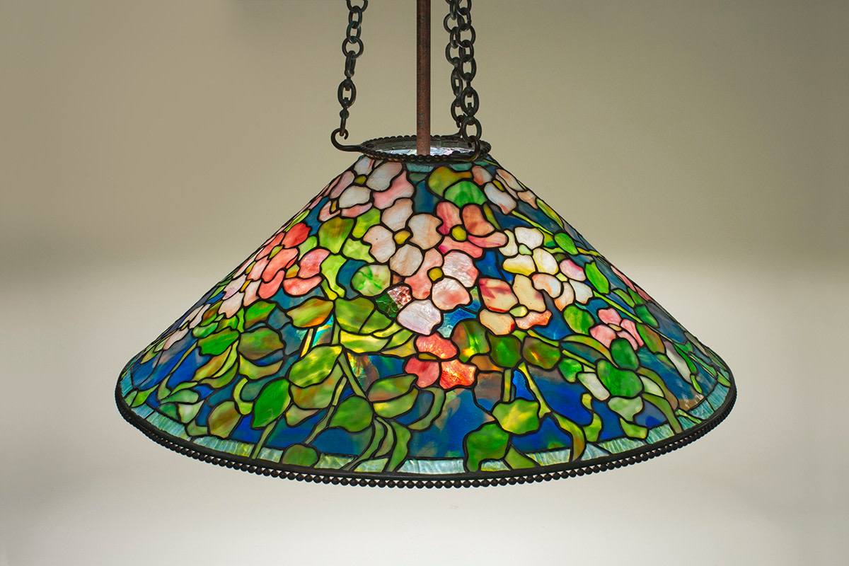 A leaded glass hanging authentic tiffany lamp shade, the conical shade depicting pink and white dogwood blossoms in opalescent tiffany glass against a variegated blue background