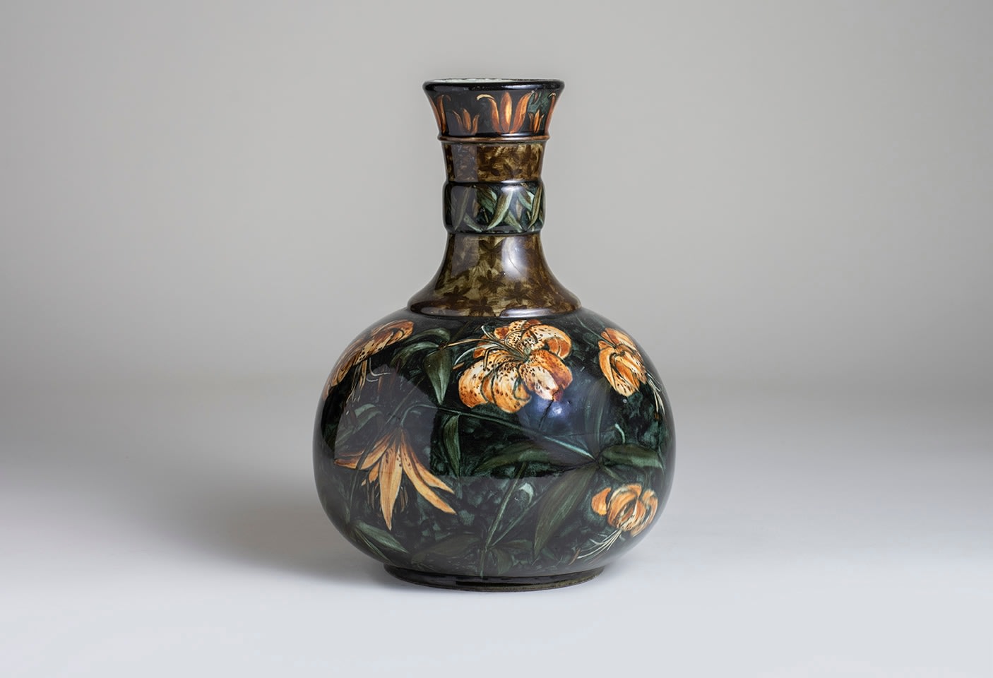 a bottle form ceramic vase with rounded body and thin cylindrical stem, with underglaze decoration of pale yellow lilies on a variegated dark green ground