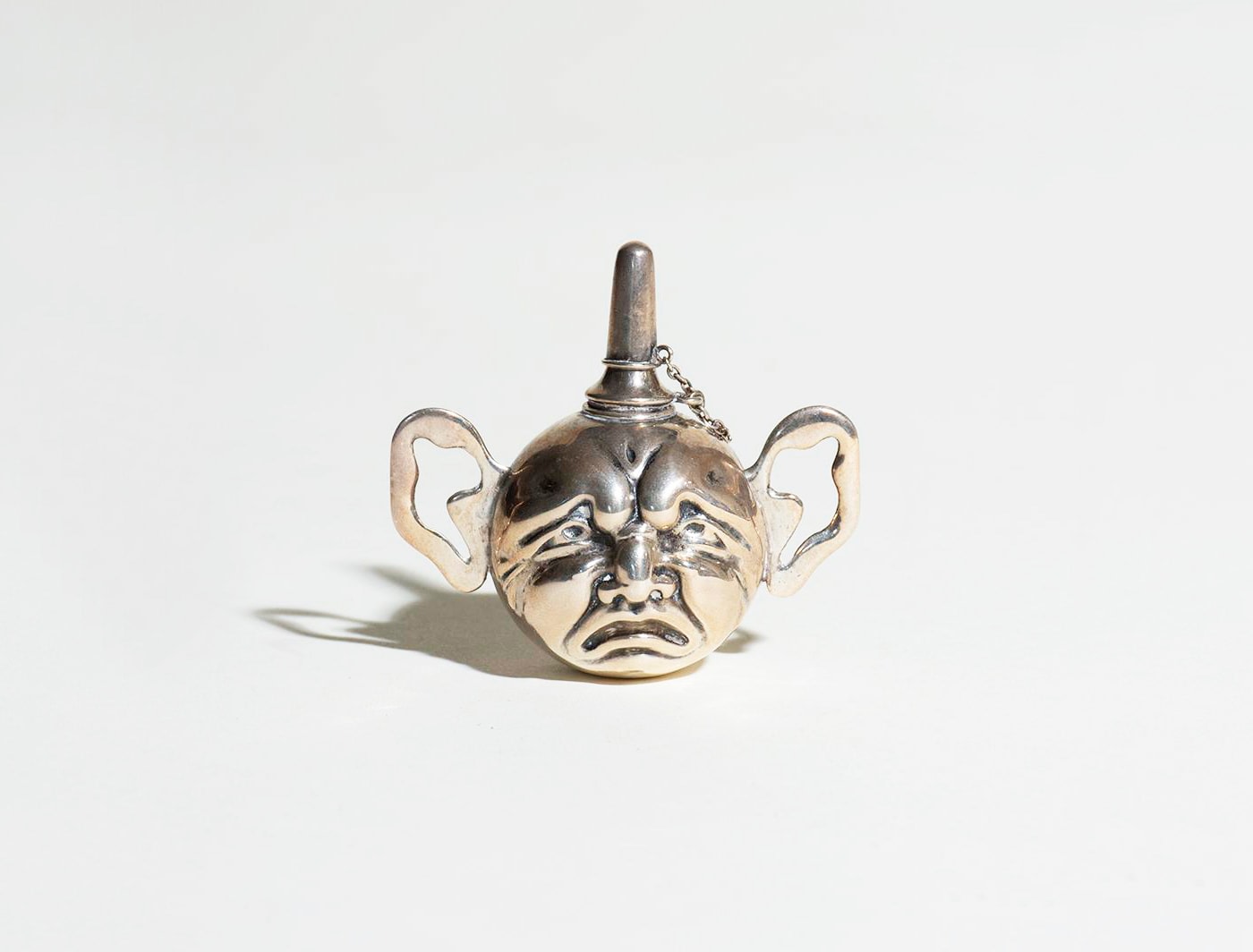 a small round old fashioned cigar lighter, the round body with relief decoration on either side of tragedy and comedy like faces, with ears for handles.