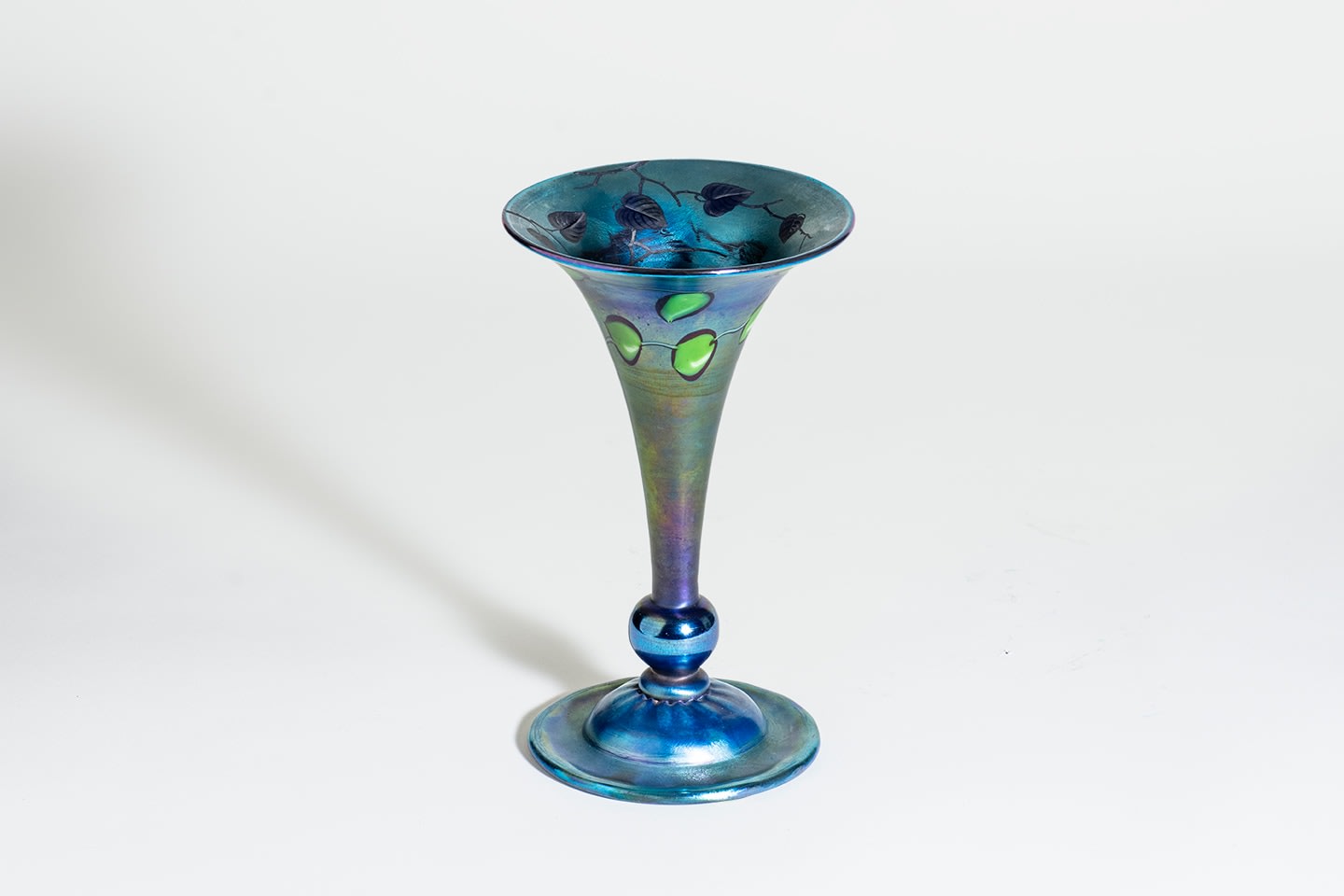 a trumpet shaped vase in deep cobalt blue iridescent tiffany glass, decorated with round green leaves and vines