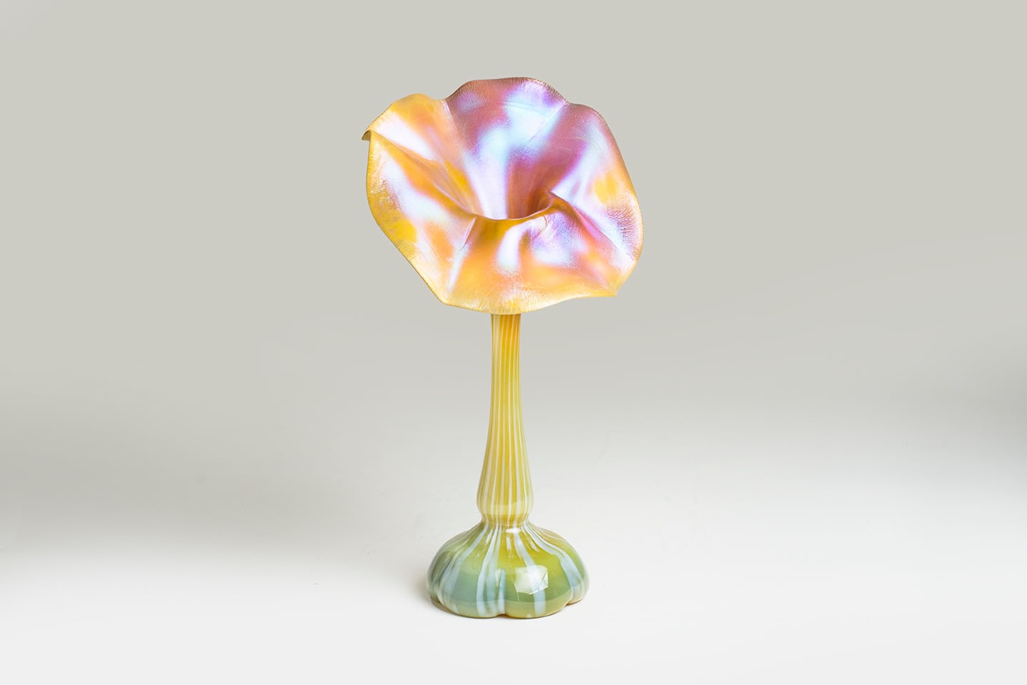 an early blown glass tiffany favrile vase, a pillowed domed foot rising to thin cylindrical stem, with a round flared flower &quot;face&quot; with sculptural waved edges, in yellow tiffany favrile glass with white striations and silvery magenta surface iridescence