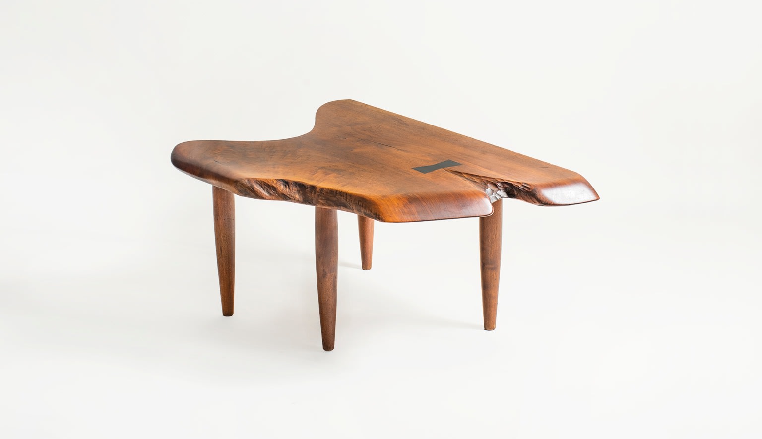 an occasional table with four tapering legs and live edge slab top of walnut with chip carved detail and ebony butterfly joint