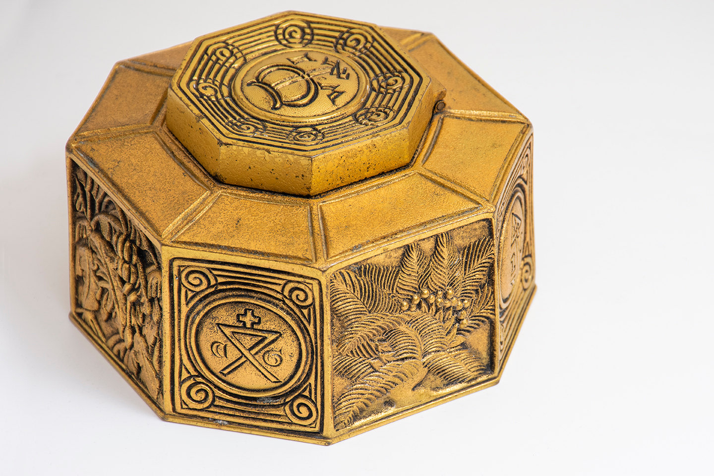 a low wide 8-sided inkwell by tiffany studios from the bookmark desk set, in gilt bronze, with decorations on the flat sides inspired by 15th century printer's marks, including botanical designs and monograms