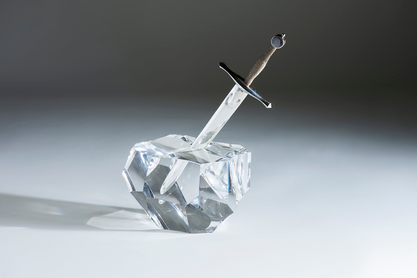 a faceted crystal paperweight in the form of a large stone, with a small recess in which a sterling silver &quot;sword&quot; with twister rope handle in 18K gold sits representing excalibur or the sword in the stone from arthurian legend