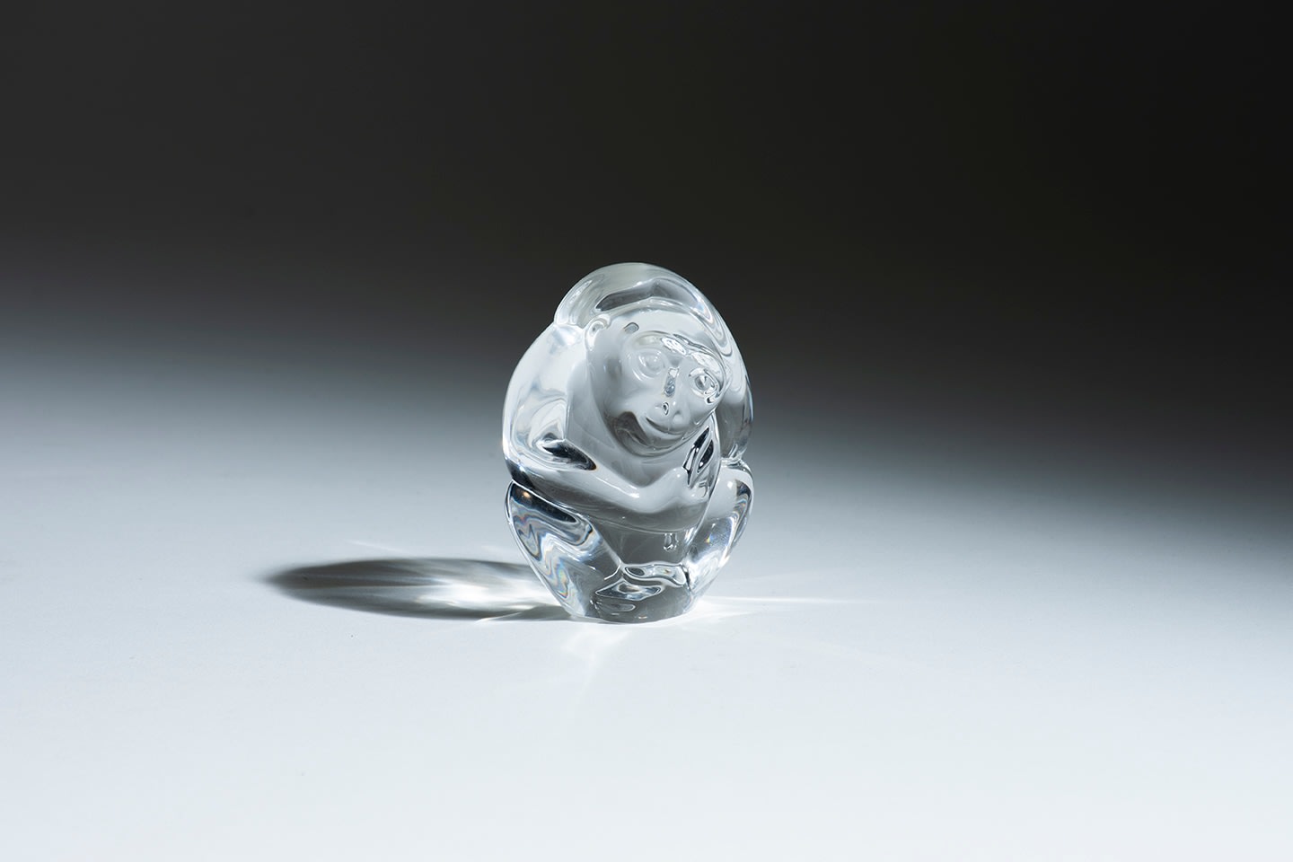 a small oval shaped sculpture in clear highly refractive crystal in the shape of a monkey, symbolizing cleverness, by american glass company steuben, meant to be held in the hand to cool down the palms