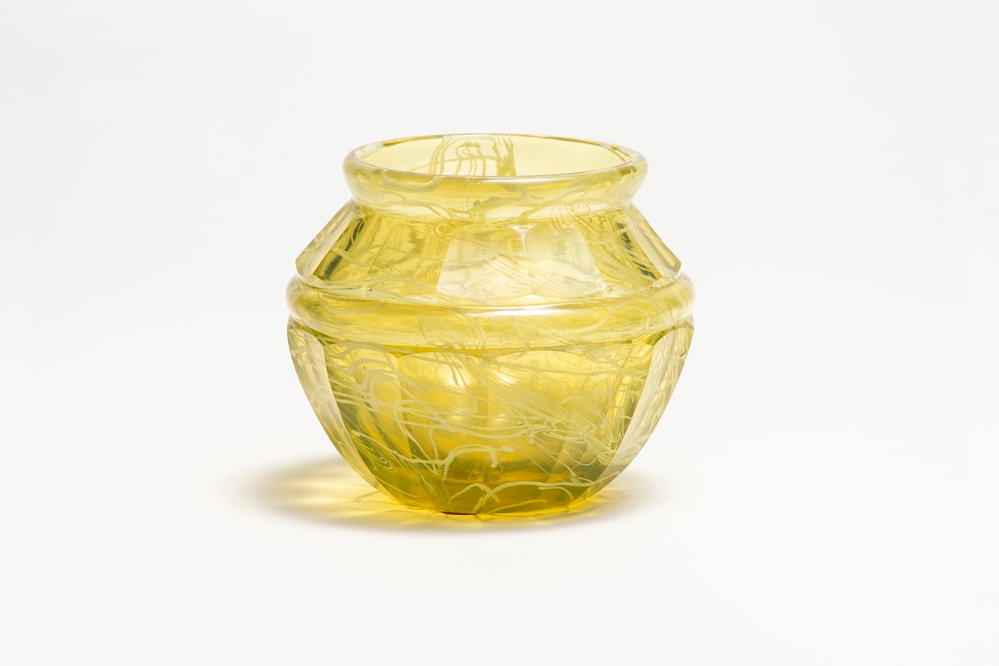a small tiffany glass vase in transparent yellow glass with internal decoration of thin abstract swirls in creamy white, the surface with hand cut facets