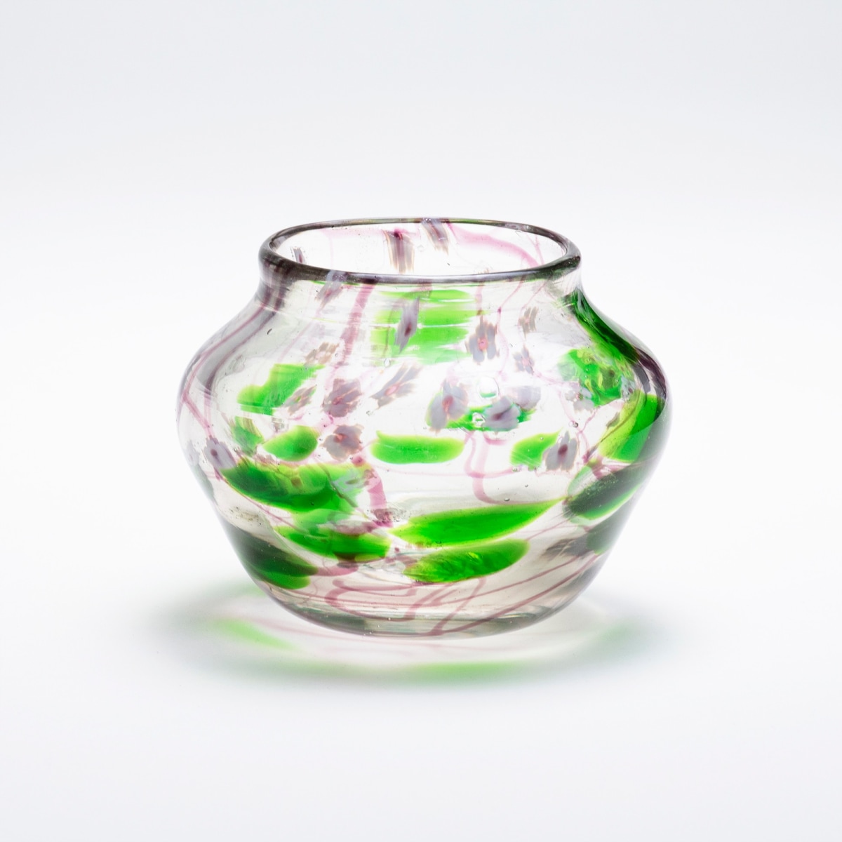 a blown favrile glass vase by tiffany studios, the irregular clear rounded body with a motif of swirling abstract thin vines in a shade of purple, with bright green round leaves interspersed throughout, with tiny white &quot;millefiori&quot; flowers.