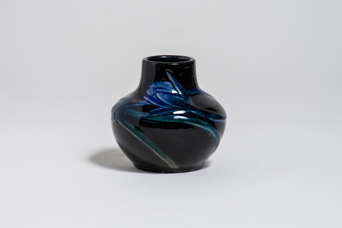a black cabinet vase with rounded body, decorated with raised relief motif of dark blue crocuses with green stems and leaves, against a black ground, with glossy clear glaze