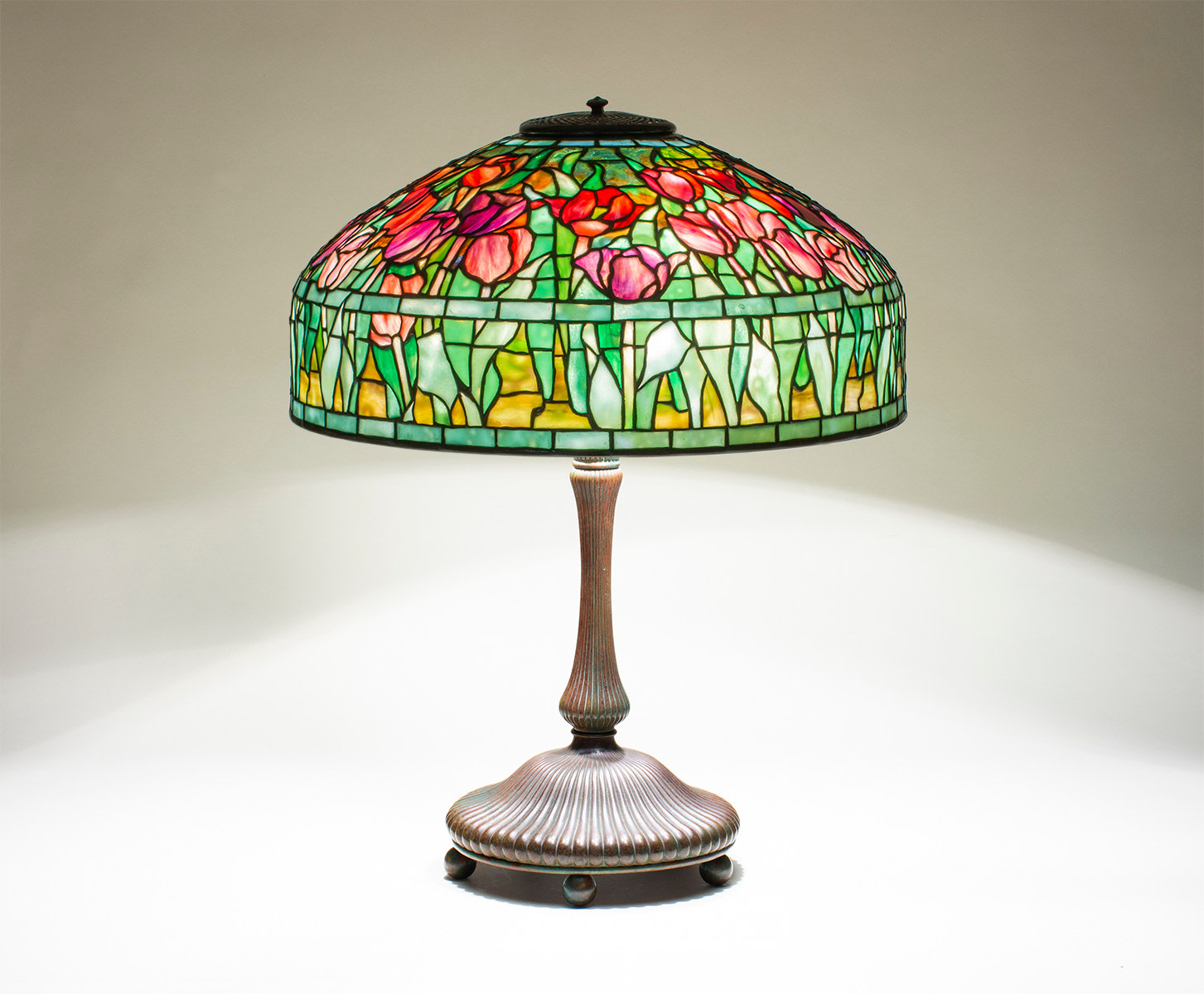 a leaded glass and bronze tiffany lamp, the shade depicting red and pink tulips in streaky glass, with mottled green leaves