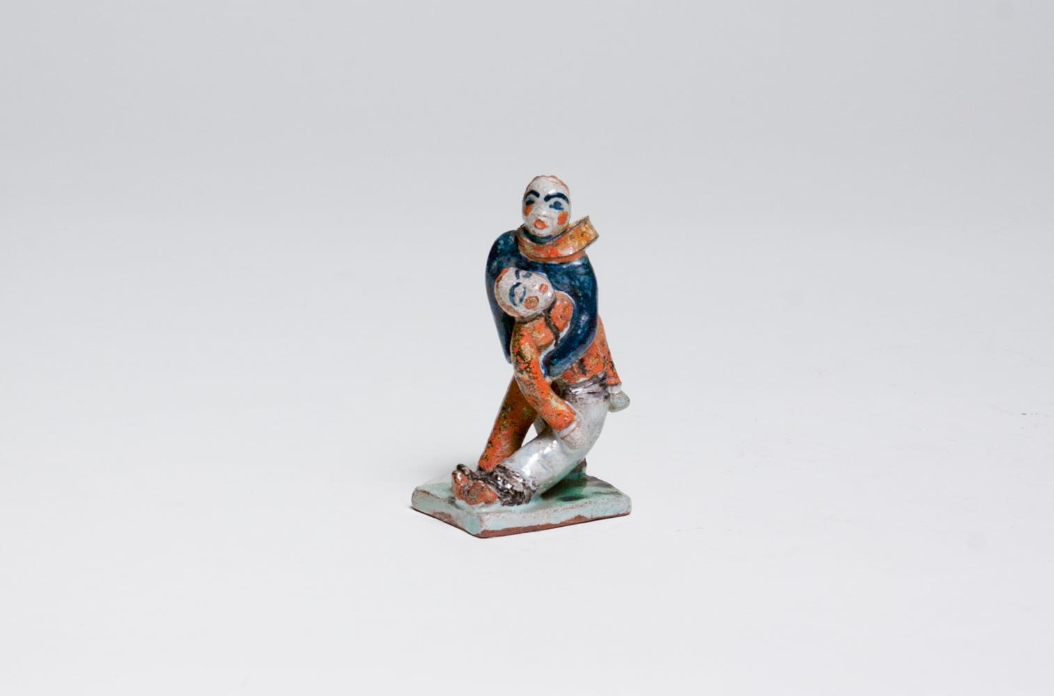 a small glazed ceramic sculpture of two figures who appear to be figure skating, one falling into the arms of the other whose scarf is blowing in the wind