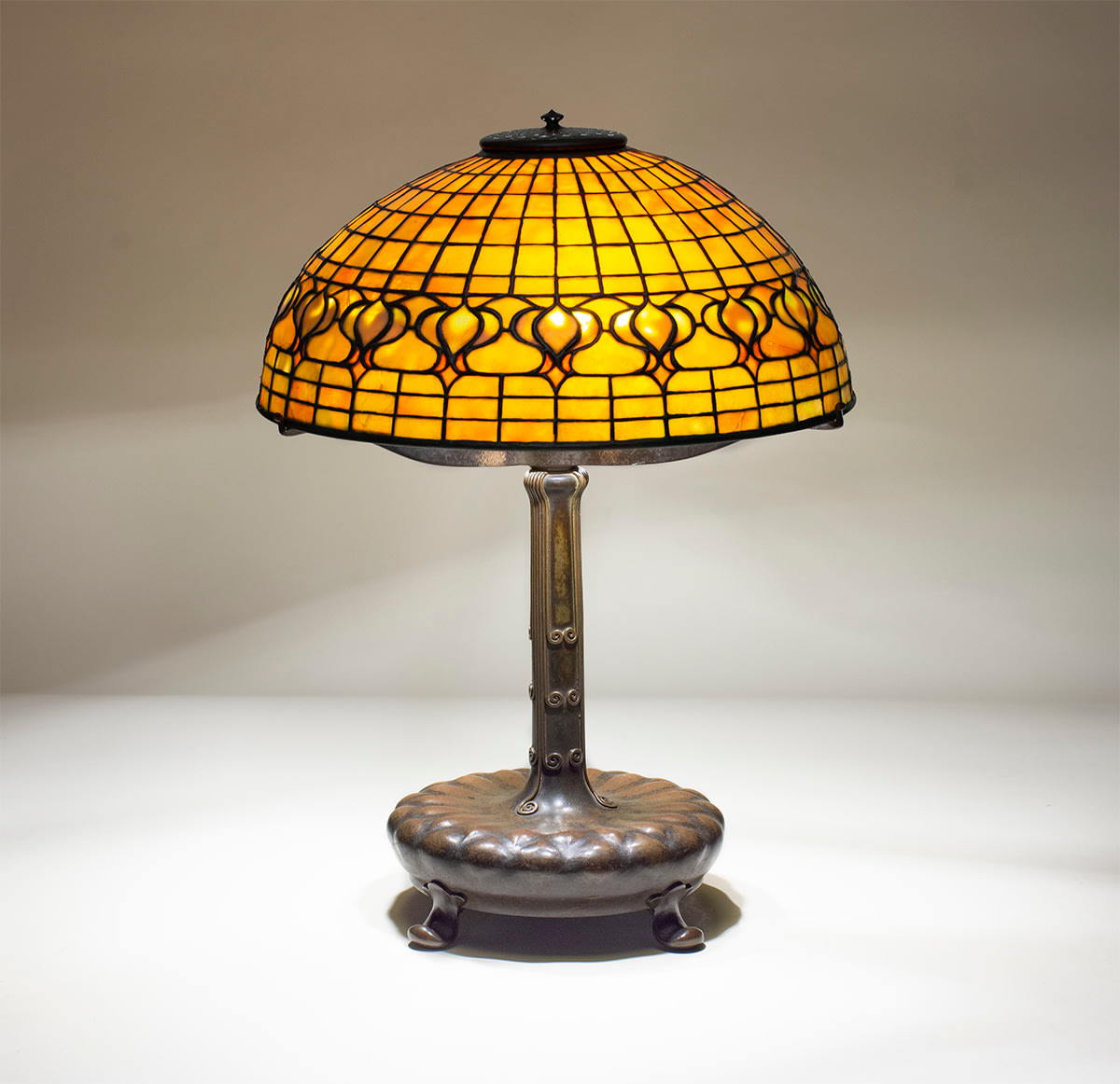 a leaded glass geometric tiffany lamp, the shade in orange tiffany glass depicting stylized pomegranates against a gridded glass backgound