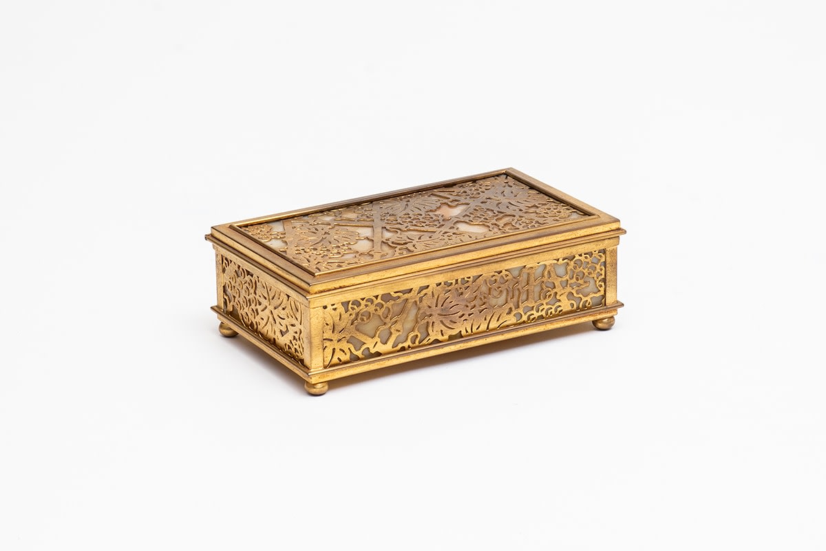 a small low rectangular box with hinged lid from tiffany studios Grapevine pattern desk set, resting on four ball feet, gilt bronze overlay of pierced metalwork showing grapevines and grape clusters and leaves, mounted over striated amber Tiffany Glass