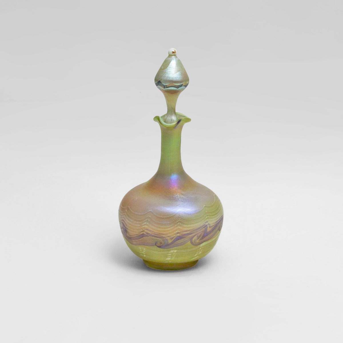 an iridescent perfume bottle by tiffany studios in pale greenish glass with matching swirling decoration on the body of the bottle and the teardrop shaped stopper