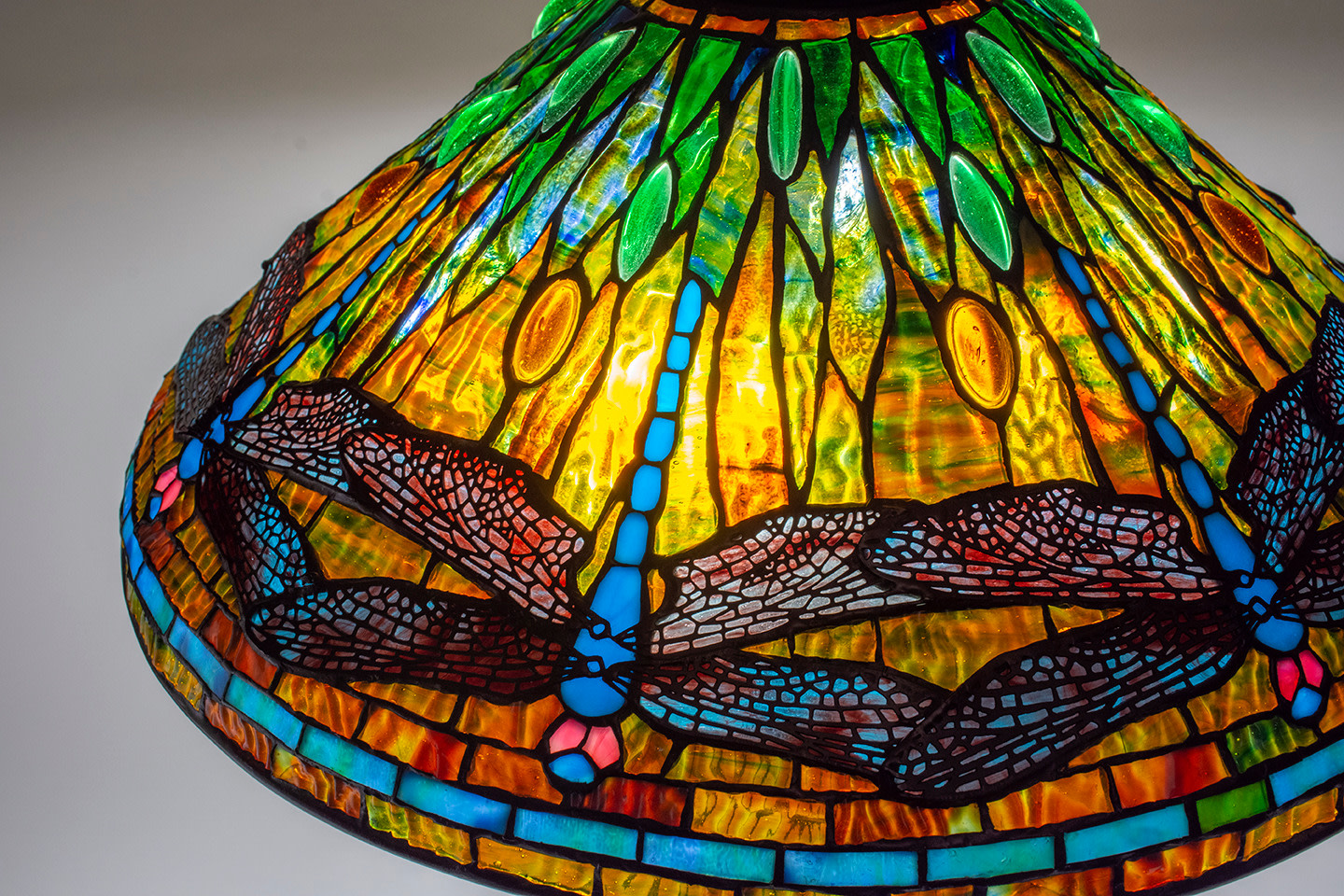 a 20-inch diameter cone-shaped leaded glass tiffany lamp shade depicting blue dragonflies with red eyes and striated blue and red wings, against a background of vibrant rippled tiffany glass in shades of orange and green