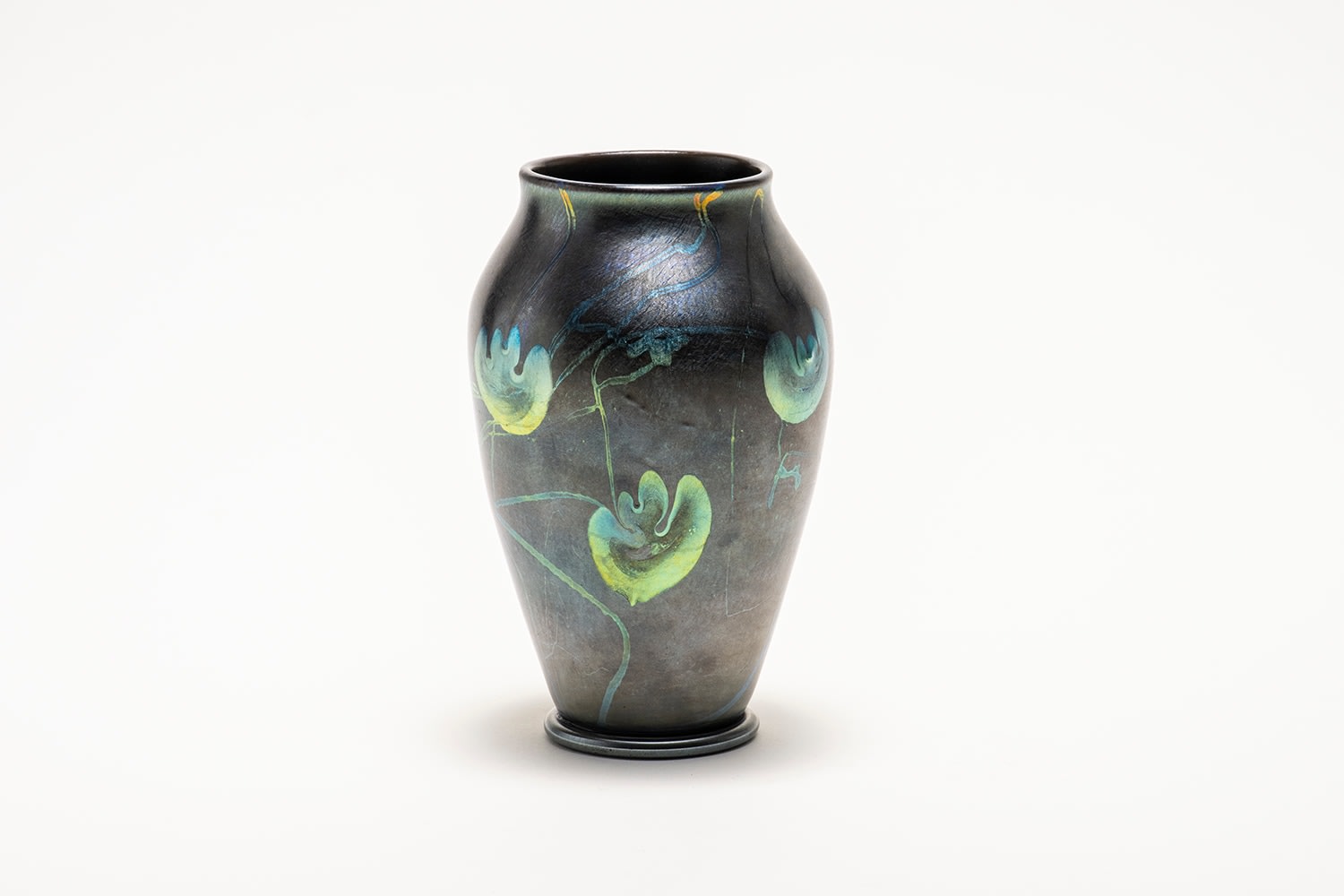 a footed tiffany glass vase in silvery gunmetal glass with iridescent decoration of swirling vines and leaves in silvery blue-green