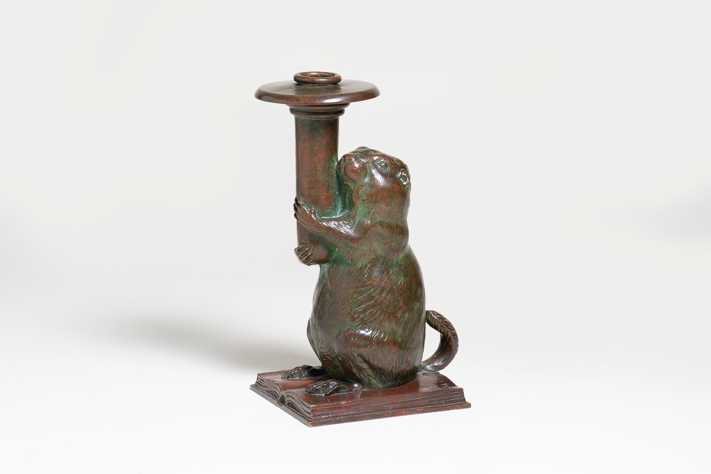 a bronze candlestick in the form of a groundhog standing on an open book, holding aloft the candle holder, by tiffany studios for the rowfant cub a cleveland bibliographic society