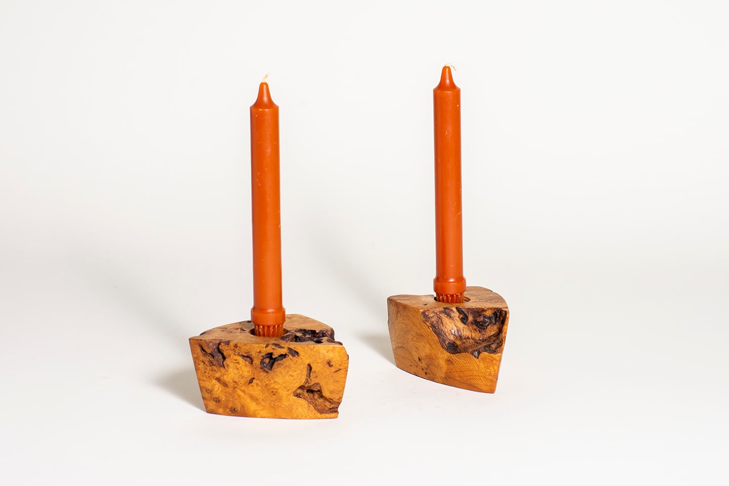 a pair of candlesticks formed by myrtle wood burl, each semi triangular in form, with highly figured grain, holding orange candles