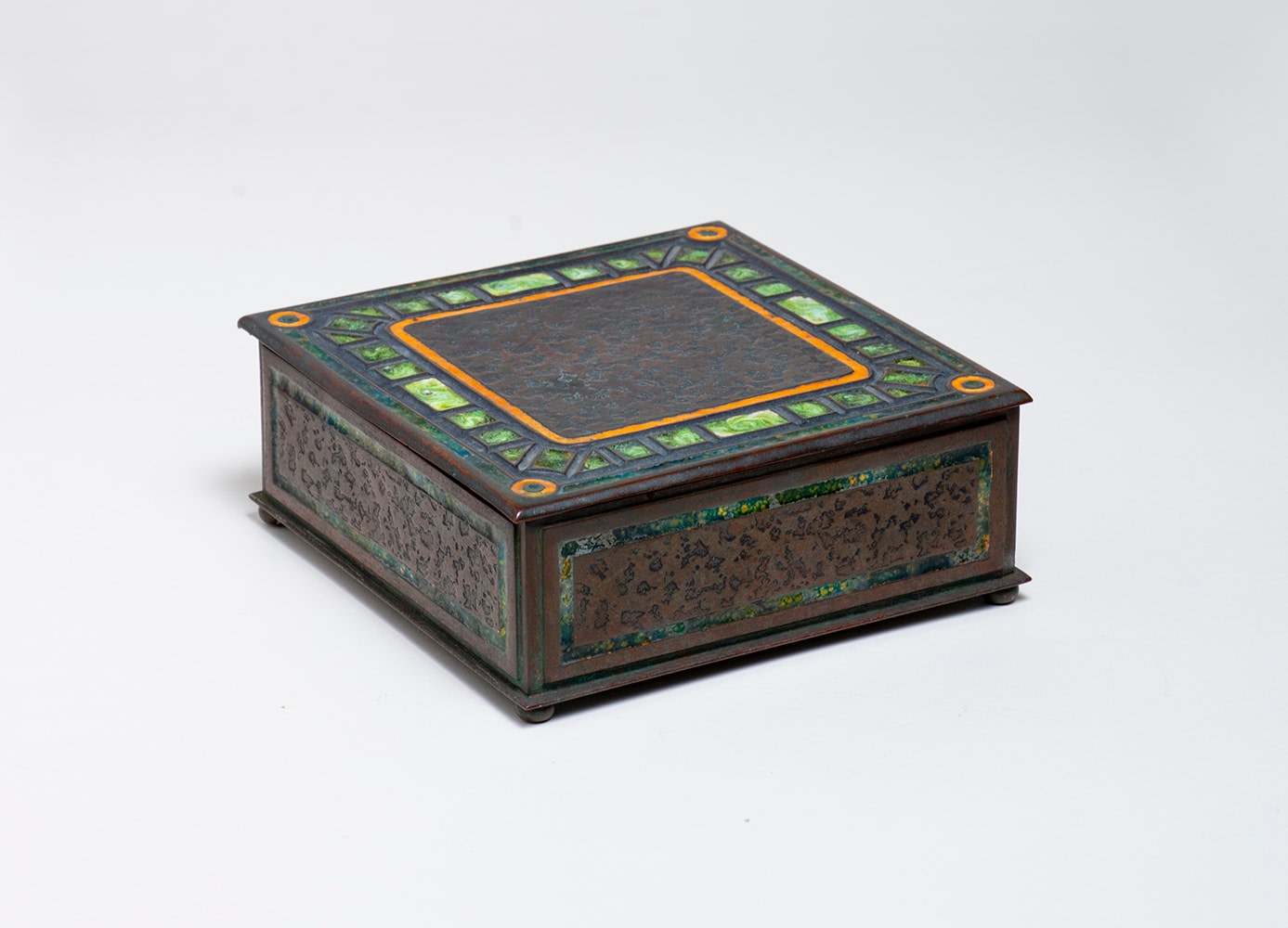 a square box from the art deco or art moderne tiffany desk set, in dark brown patina, the hinged lid with border of small rectangular motifs inset with variegated green enamel, the inside lined with cedar