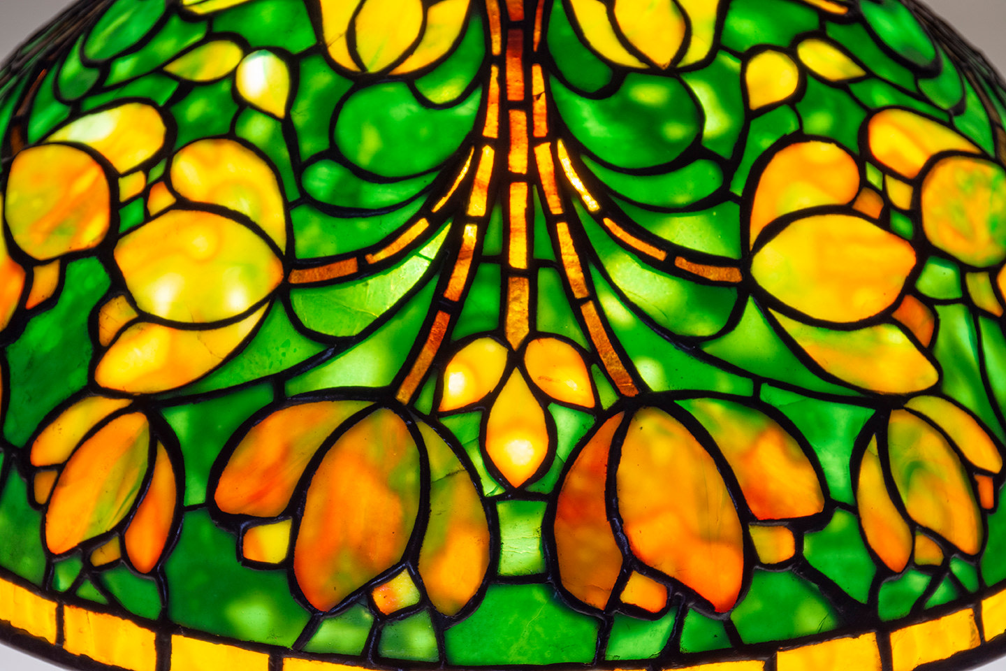 a leaded glass tiffany lamp shade with mottled green background with a bunch of variegated yellow orange tulips with hints of pale green