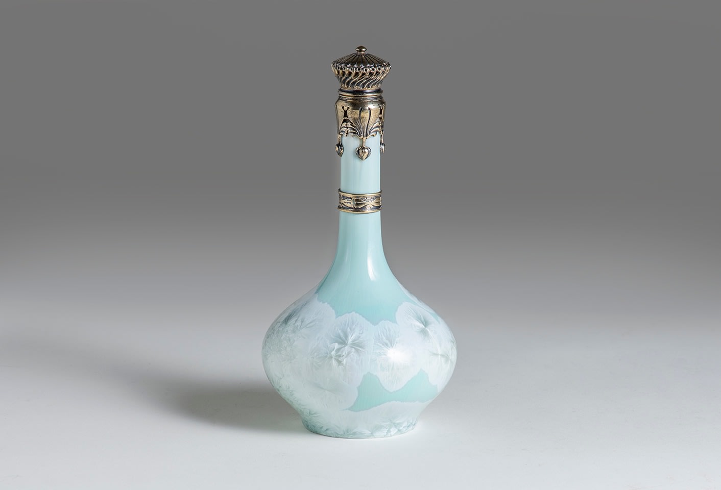 a perfume bottle, glazed in glossy aqua blue, the bottom with white crystalline glaze, with a silver gilt topper in art nouveau style with swirling decoration