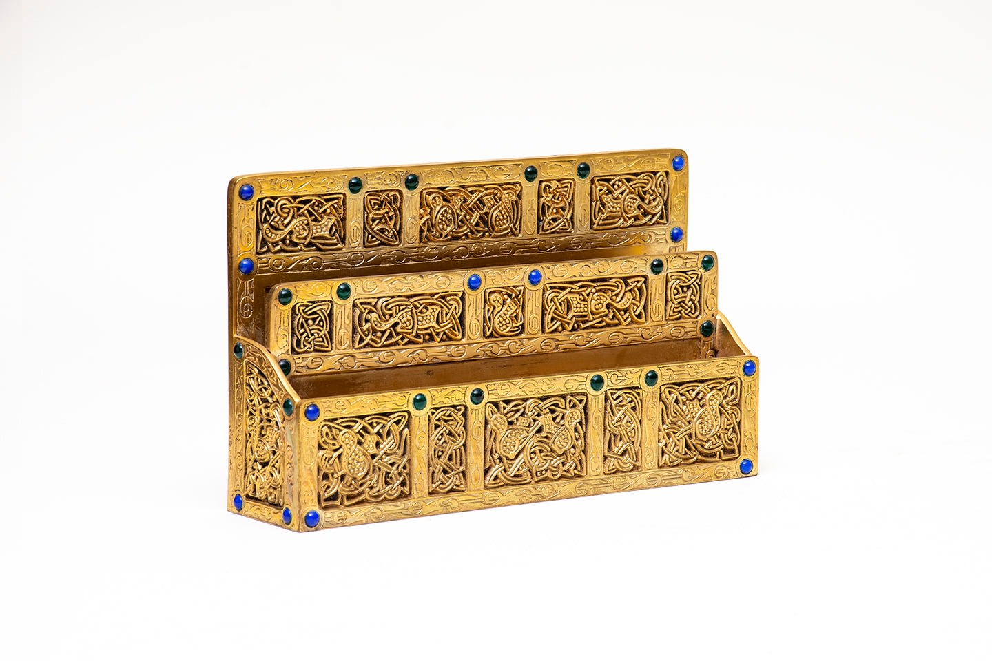 a gilt bronze letter rack with stylized carved decoration on flat planes in medieval style depicting animals like hares and squirrels, surrounded by elaborate strapwork and knotwork decoration, with small rounded glass jewels in blue and green