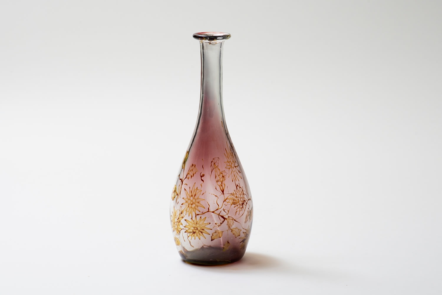 a bottle form vase in the graal technique by swedish glass company orrefors, the clear glass with sections of transparent deep purple, decorated with a motif of golden flowers and leaves