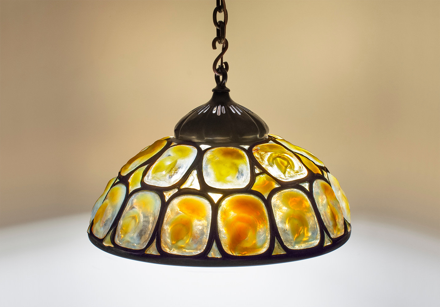 a monumental hanging shade by tiffany studios comprising a series of leaded tiffany glass &quot;turtle back&quot; tiles, each measuring over 6 inches in length and 4 inches in width, in gold iridescent glass, their irregular surfaces and shapes recalling the shell of a turtle.