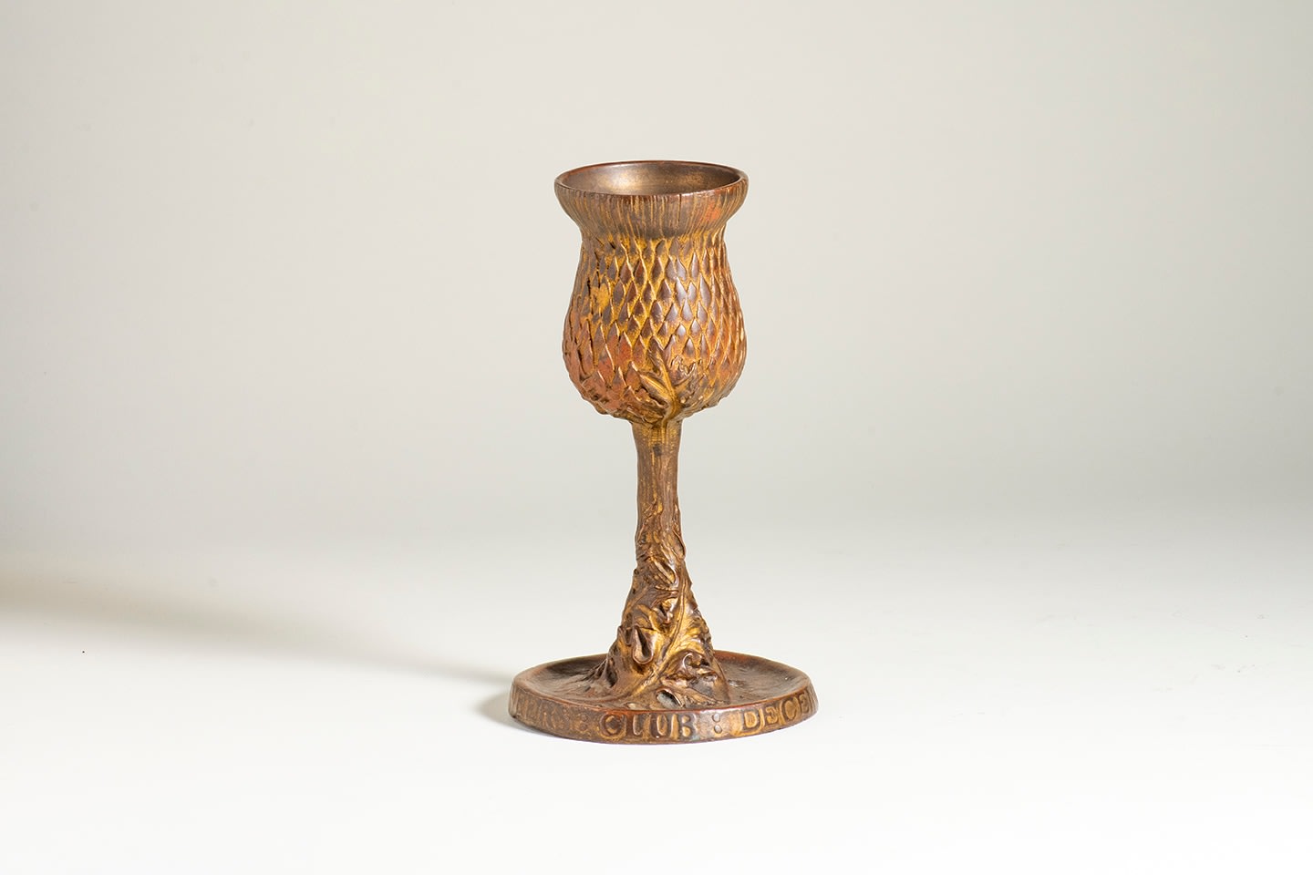 a bronze goblet with remnants of gilding, in the form of a thistle bud, with leaves curving around the stem, the round foot with information about the dinner it was made for in December 1907