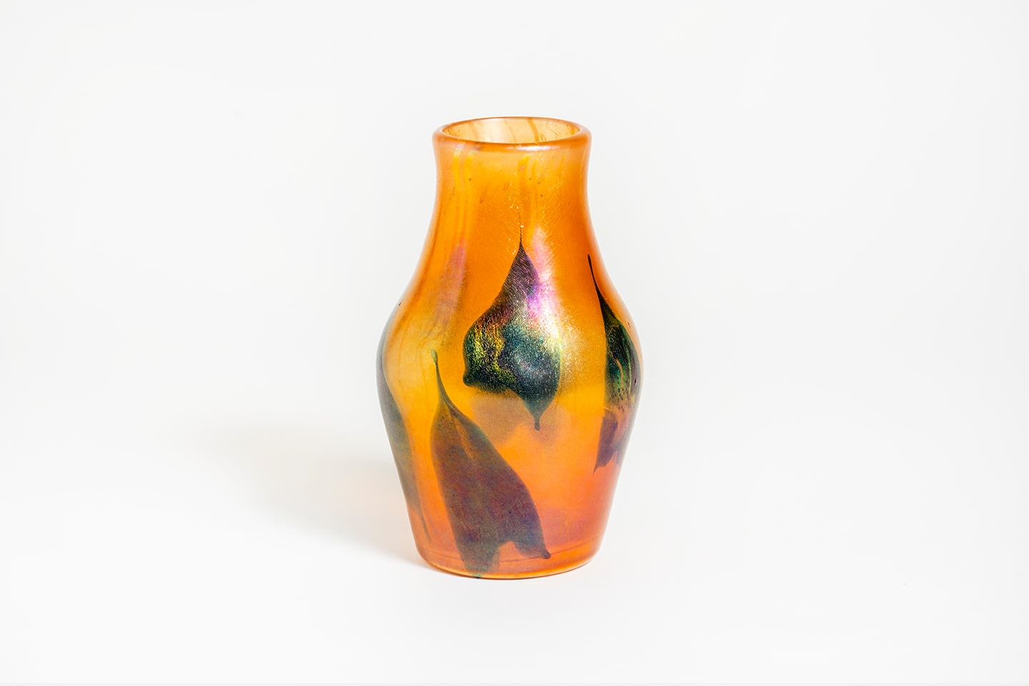 an orange translucent vase with decoration on the surface of abstracted trilobed pointed arrowhead leaves, the leaves in a dark glass called Cypriote by Tiffany because of the irregular surface texture and rainbow iridescence which imitated ancient glass