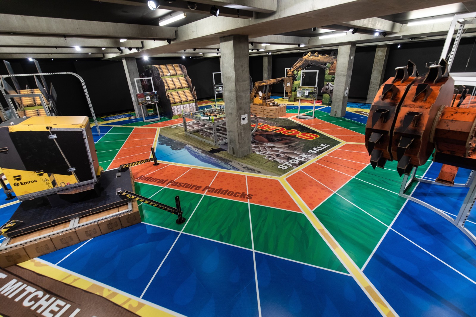 installation of MINE at MONA in 2020, featuring large vinyl on the floor that looks like a board game and several large cardboard sculptures of mining machinery standing on it.