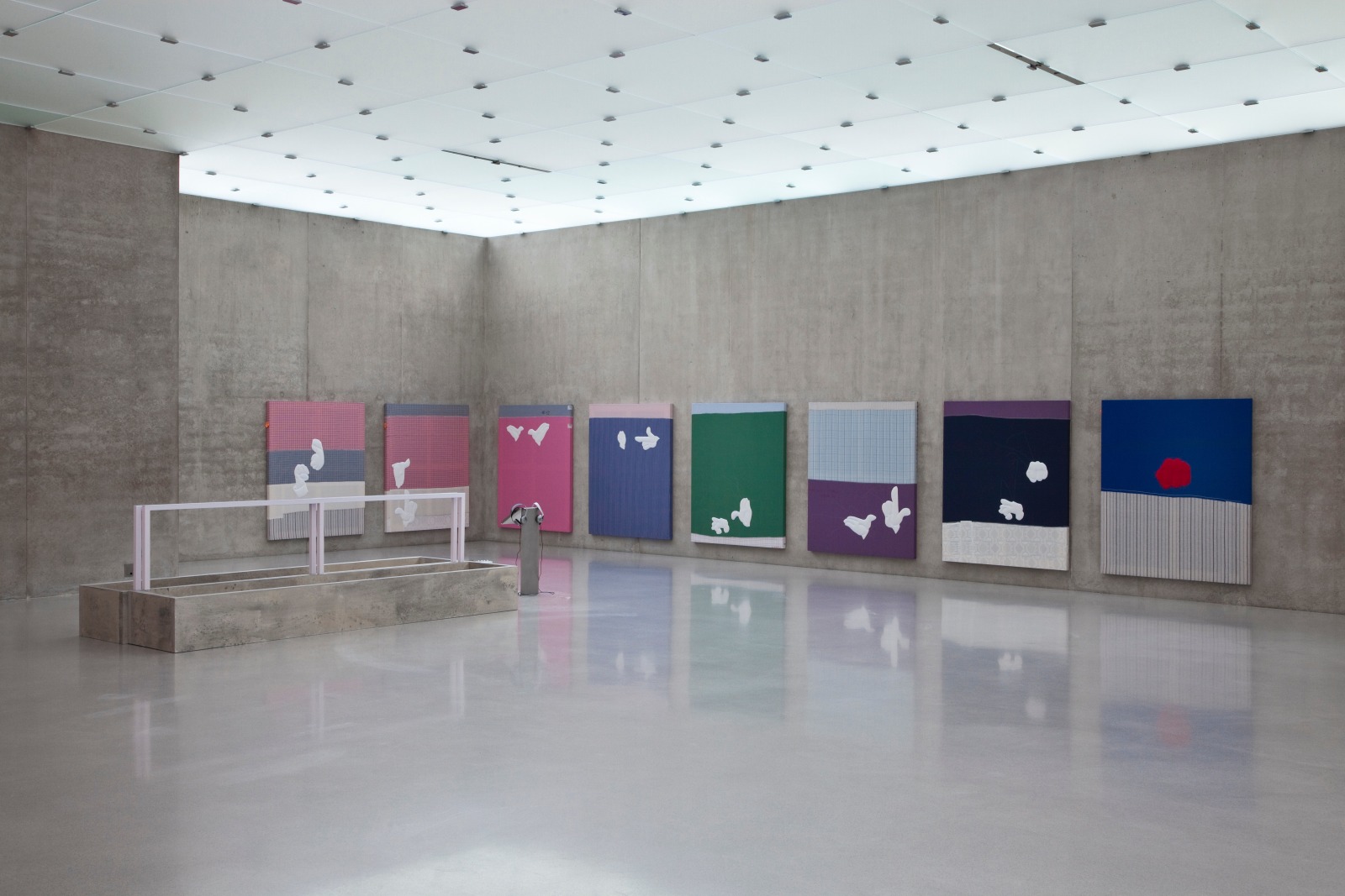 Installation view from Kunsthaus Bregenz in 2010. Eight textile paintings hang on two perpendicular walls. All are different colors and feature white gloved hands embroidered on them.