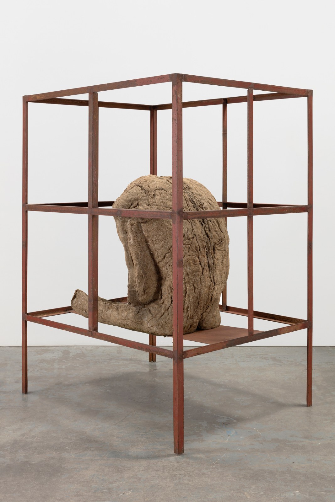 Sculpture of a life-size seated burlap and resin figure in an iron cage by Magdalena Abakanowicz