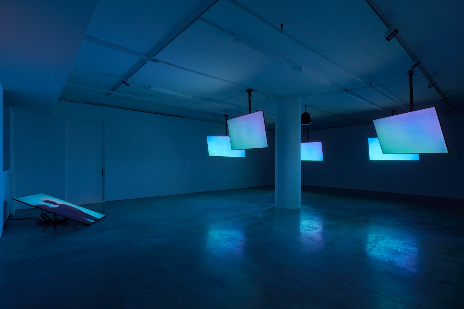 Photo of the installation by Le'Andra LeSeur containing five ceiling monitors and one floor monitor displaying shades of blue