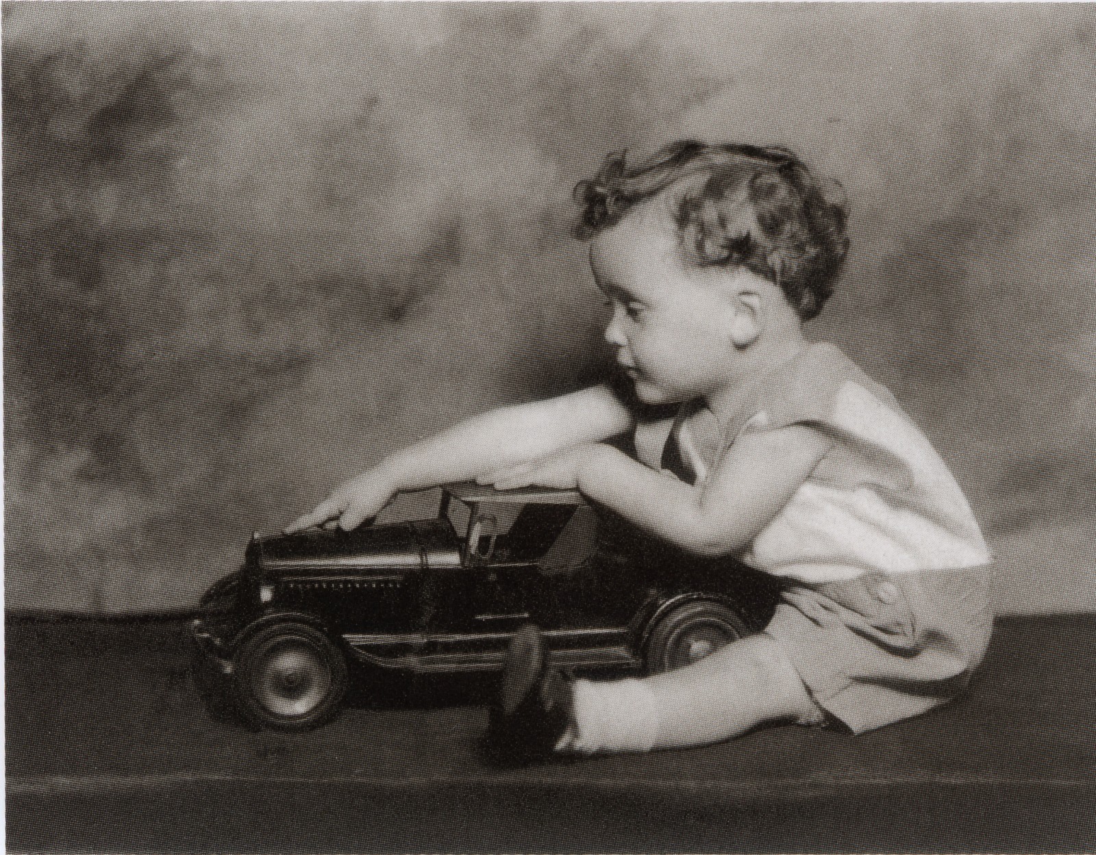 A black and white photograph of Robert Clark as a young child playing with a toy car