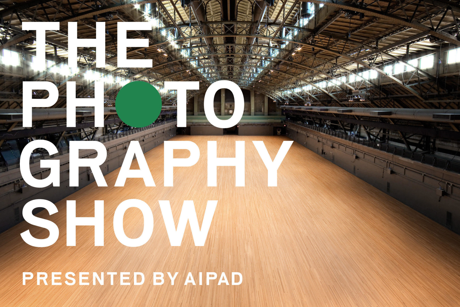 The empty Drill Hall of the Park Avenue Armory with THE PHOTOGRAPHY SHOW logo on the left side. The first O in PHOTO is replaced by a green dot.