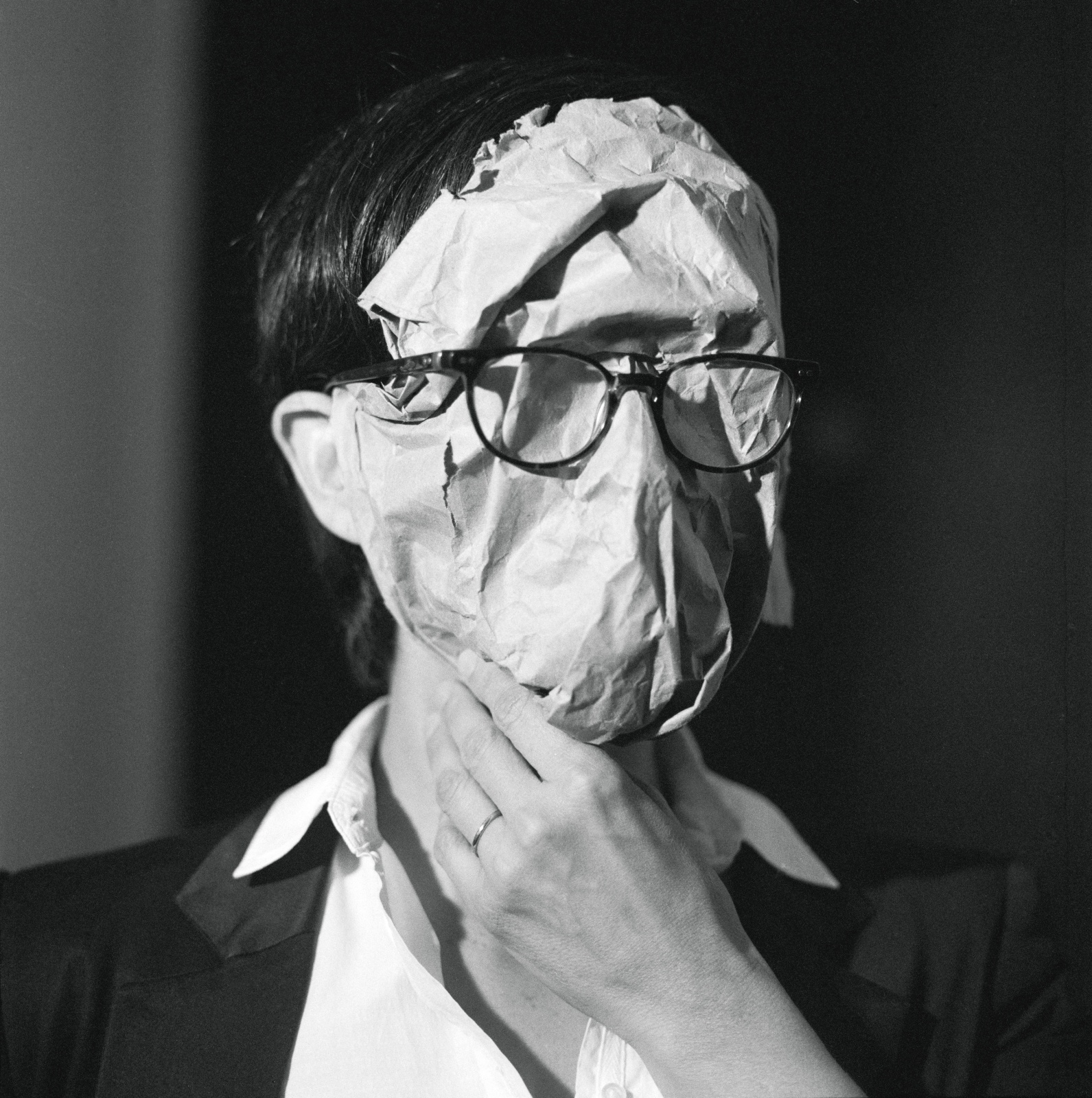 A person with a piece of paper affixed to their face wears eyeglasses on top of the paper.