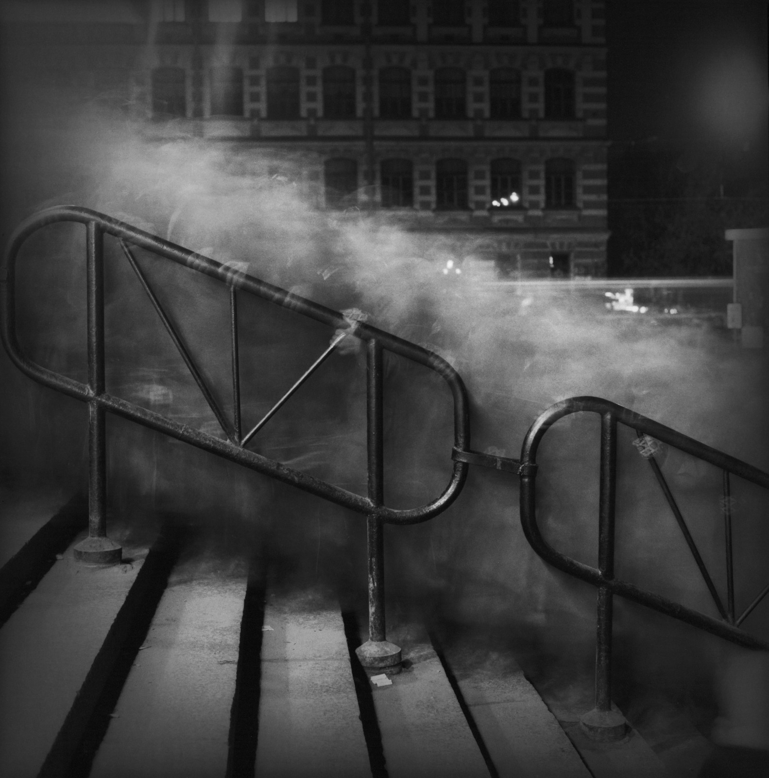 A time-lapse image of blurry figures going up a staircase at night in a black and white photo