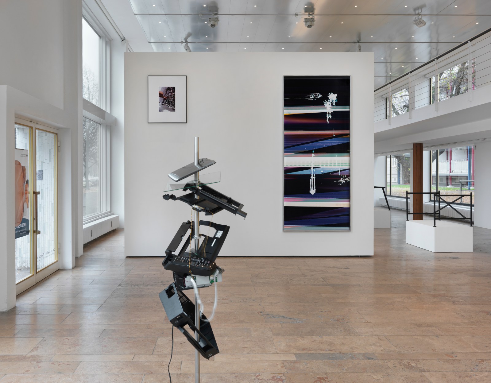 Installation view of Beshty's exhibition at Capitain Petzel featuring a deconstructed computer work in the center of the floor and a large black curl piece on the wall in the background.