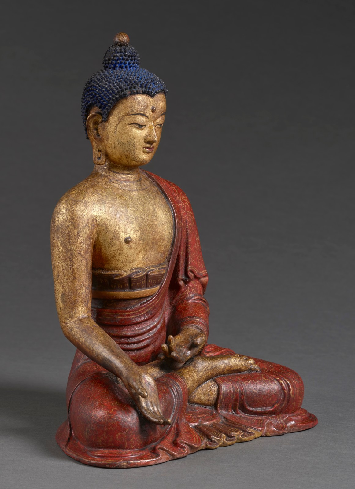 Angled view of a rare gilt and polychrome lacquered clay sculpture shows the tathagata Ratnasambhava seated in dhyanasana with his hands displaying varada and dhyana mudras. 