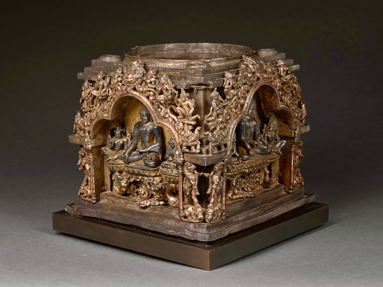 Same image of This plinth from an important eastern Indian stupa is assembled from four separately-cast gilt-copper arches (torana) with crouching elephants, rampant leogryphs, and jewel-topped pillars supporting trilobate spans, makara at either end of the crossbars, bodhisattvas and celestial figures above, and with kirtimukha at the apex.  
