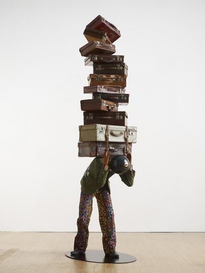 mannequin with a globe for a head carrying multiple suitcases on his back