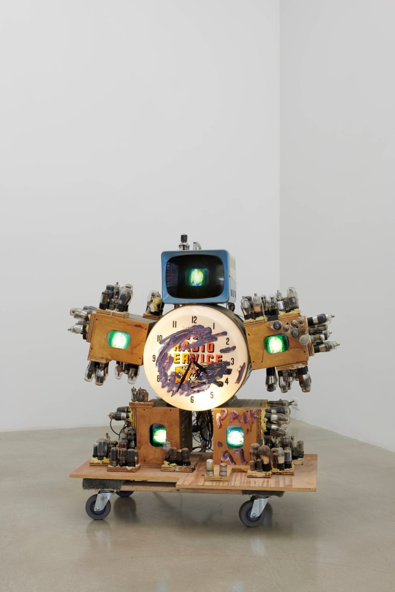 Five small televisions mounted around a clock, on wheels