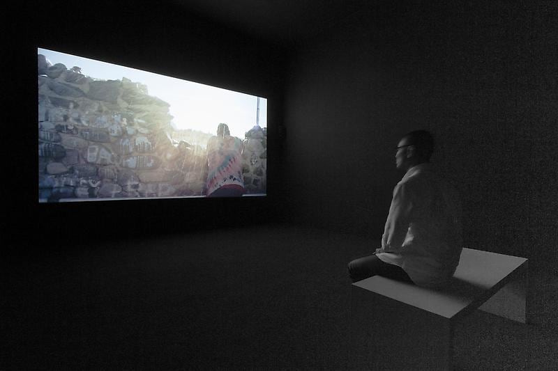 man seated on a bench looking at a video projection