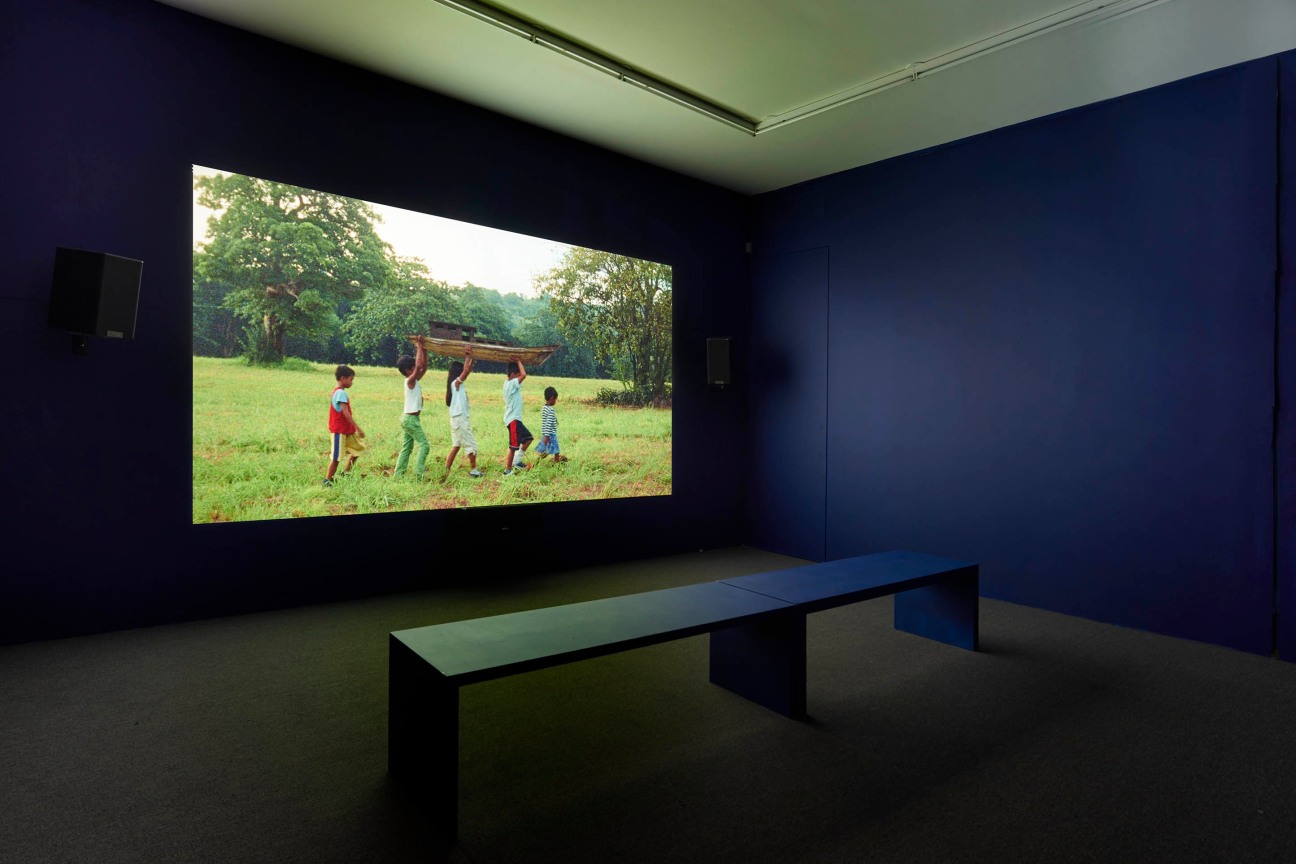 a dark room with a video projection showing children carrying a wooden boat